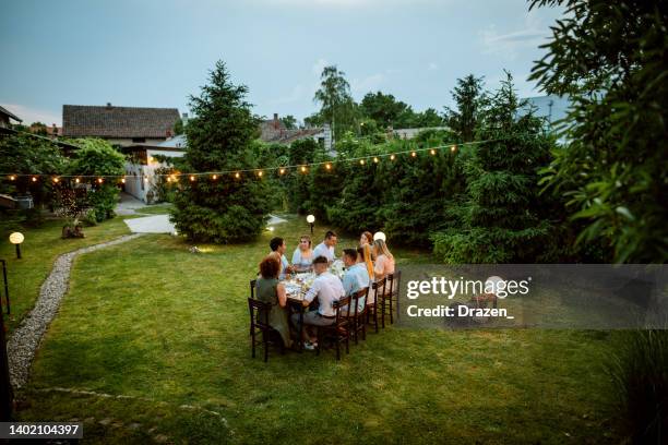 foto gran angular de personas cenando al aire libre en verano. gran grupo de amigos y familiares comiendo en un bonito jardín - fiesta de jardín fotografías e imágenes de stock