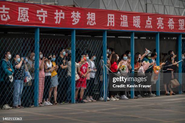 Parents and relatives, some holding flowers, wait for students to emerge after finishing the final day of the National College Entrance Examination,...