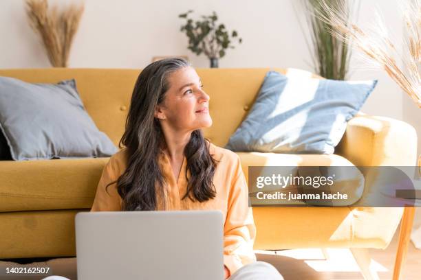mature woman sitting at home with laptop smiling at photos of her grandchildren on social media. - casa real española fotografías e imágenes de stock