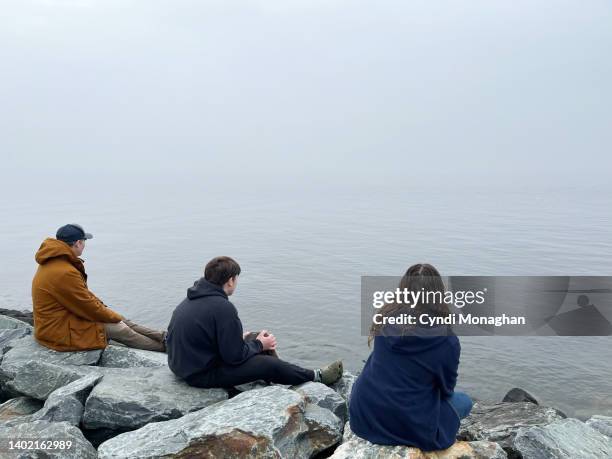 family gathered on a rocky beach at the water's edge while hiking together on tilghman island. chesapeake bay on a winter day. road trip rest stop. weekend getaway to tilghman island. - tilghman stock pictures, royalty-free photos & images