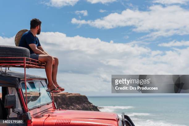 tourist contemplating the beach in off road car - 4x4 stockfoto's en -beelden