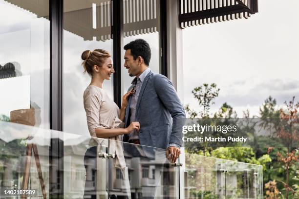 young multiracial couple standing on balcony of modern townhouse on suburban housing estate - capital architectural feature - fotografias e filmes do acervo