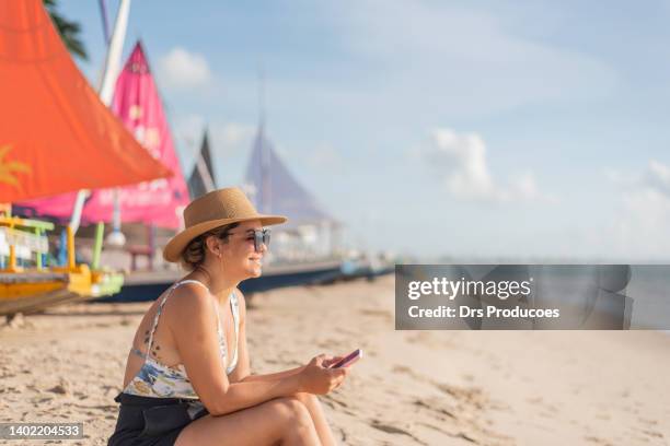 mujer sentada en la arena de la playa usando el teléfono celular - porto galinhas fotografías e imágenes de stock