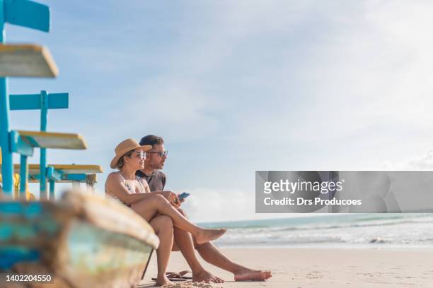 tourist couple using smartphone on the beach - 45 couple stockfoto's en -beelden
