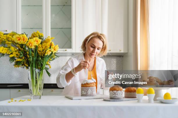 a woman in the kitchen decorates easter pastries. - paastaart stockfoto's en -beelden