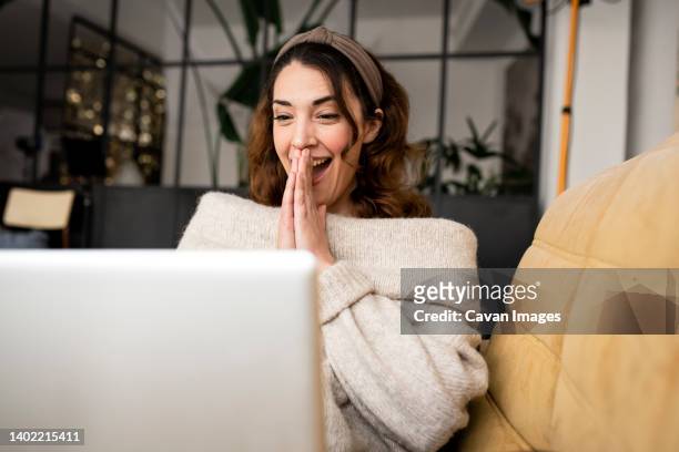 excited woman looking at laptop screen sitting on cozy sofa at home - entusiasmo fotografías e imágenes de stock
