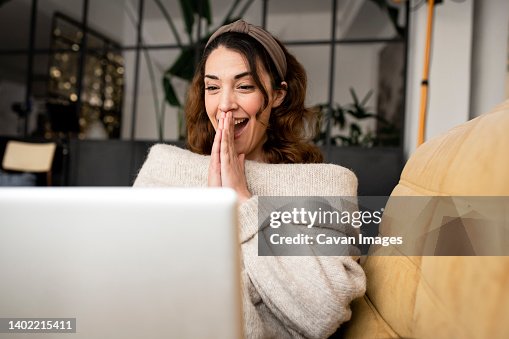 Excited woman looking at laptop screen sitting on cozy sofa at home Excited woman looking at laptop screen sitting on cozy sofa at home