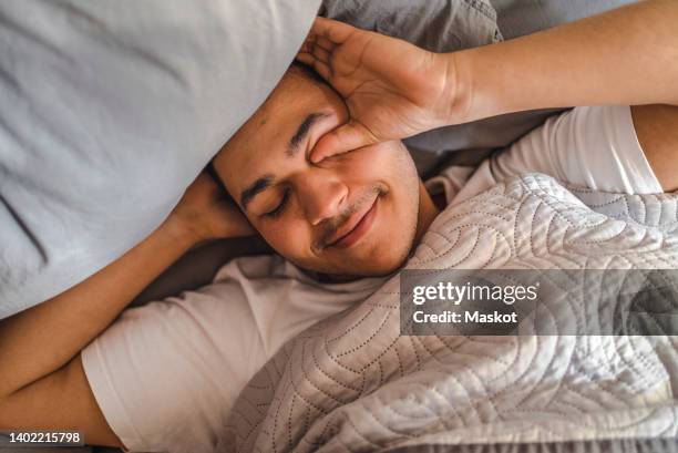 lazy man rubbing eyes while lying on bed at home - morning stock-fotos und bilder