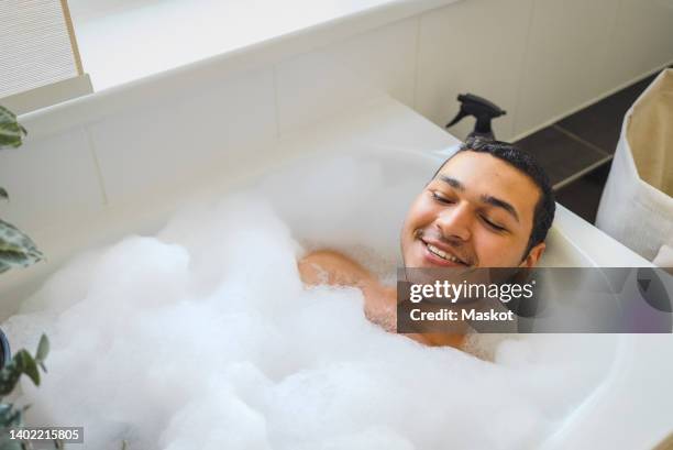 high angle view of smiling man taking bath in bathtub at home - bañera hombre fotografías e imágenes de stock