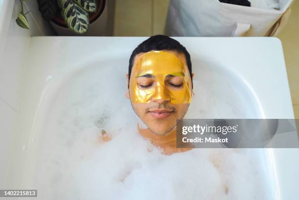 high angle view of man with facial mask relaxing in bathtub at home - kosmetikmaske stock-fotos und bilder