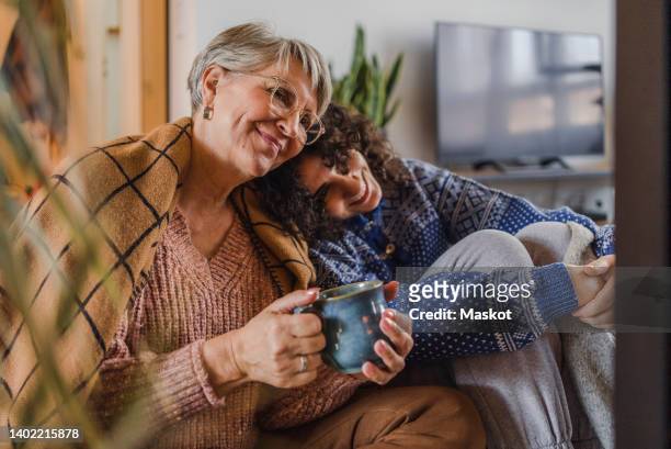 happy senior woman with coffee cup sitting with granddaughter at home - young woman with grandmother stockfoto's en -beelden