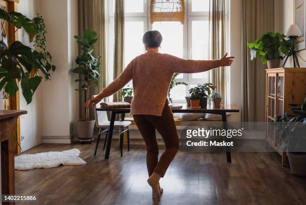 rear view of senior woman dancing in living room at home - arms outstretched fotografías e imágenes de stock