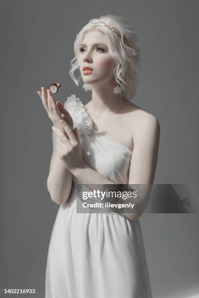 junges blondes model im studio. frau mit schöner luxuriöser griechischer frisur im weißen kleid. mädchen mit schmetterling zur hand. goldener kranz. albino. schönheitsporträt. griechische göttin. reinheit und unschuld - europe bride stock-fotos und bilder