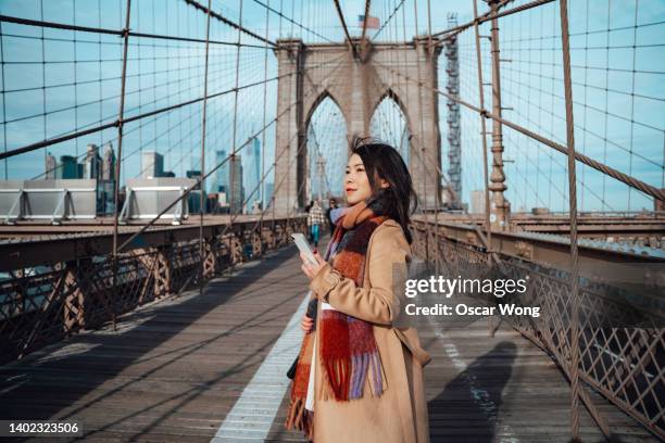 young woman using smart phone while standing on brooklyn bridge - touristen brooklyn bridge stock-fotos und bilder