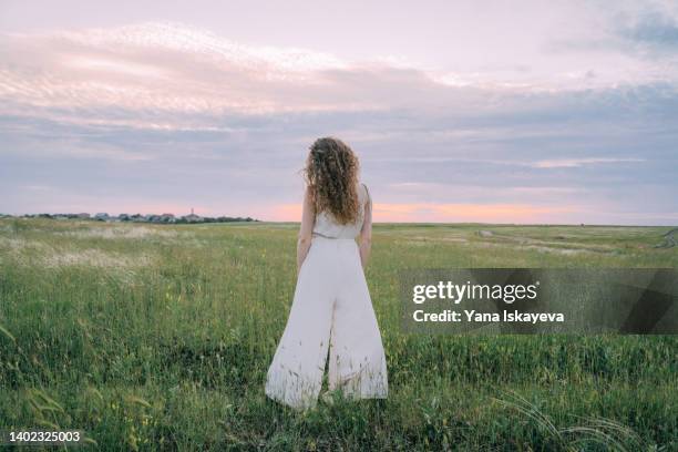 tender woman with curly hair standing in the field - white jumpsuit stock pictures, royalty-free photos & images
