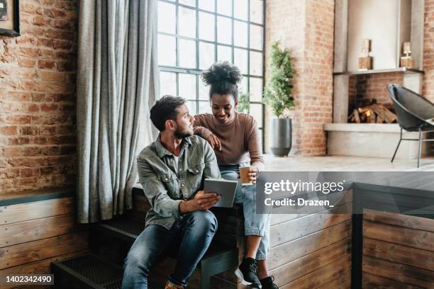 couple multiracial dans un loft moderne utilisant des technologies. couple utilisant une tablette numérique pour les applications de maison intelligente, les services bancaires électroniques et jouer à des jeux vidéo ensemble. - men stock photos et images de collection