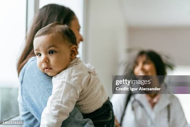 mère avec bébé sur ses genoux pour un rendez-vous médical - pédiatre photos et images de collection