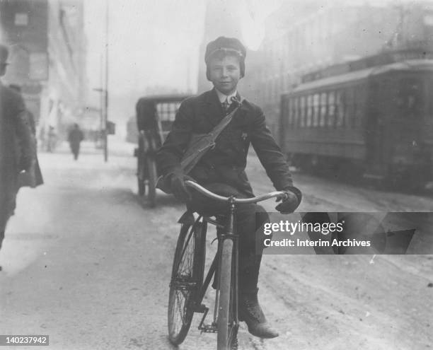 View of a young boy, posed upon his bicycle, who sells newspapers in the morning, during school hours, in Syracuse, NY, February 1910.