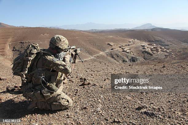 u.s. army soldier provides security for infantry patrolling through dandarh village, afghanistan. - afghanistan war fotografías e imágenes de stock