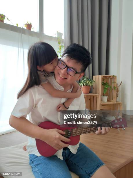 man playing ukulele with daughter at home - fashionable dad stock pictures, royalty-free photos & images