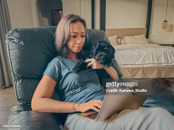 donna asiatica matura che usa il laptop mentre tiene il suo cucciolo - mature asian woman candid foto e immagini stock