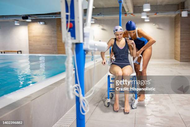 physical therapist helping a patient enter the pool on a hoist chair - aquatic therapy stockfoto's en -beelden