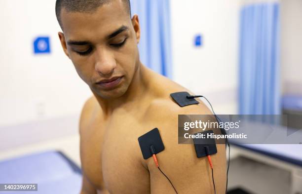 mann in der physiotherapie, der eine elektrische stimulationstherapie auf seiner schulter erhält - sportmedizin stock-fotos und bilder