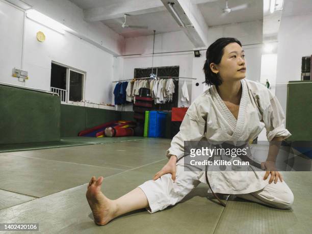 asian woman in karate gi stretching in a dojo - women's judo fotografías e imágenes de stock