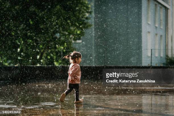 a photo of a toddler girl playing in the summer rain - shower water stockfoto's en -beelden