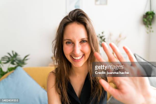 woman smiling at camera while waving her hand saying hello to someone. - skype call stock pictures, royalty-free photos & images