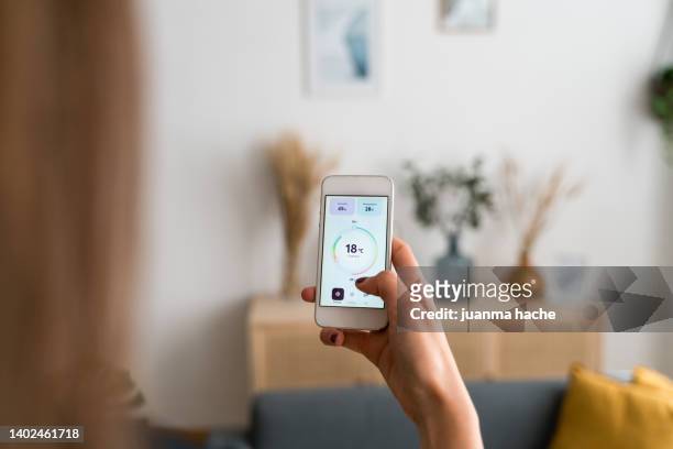 woman using an app on the mobile phone to setting the temperature indoors at home. - アクセス ストックフォトと画像