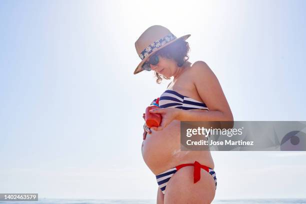 pregnant woman on the beach putting sunscreen on her belly - putting lotion stock pictures, royalty-free photos & images