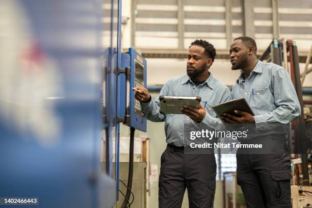 manpower and skill implications of technical change in the engineering industry. a male african american production supervisor explaining of injection molding machine structure to his operator in the plastics auto parts production line. - injection molding stock pictures, royalty-free photos & images