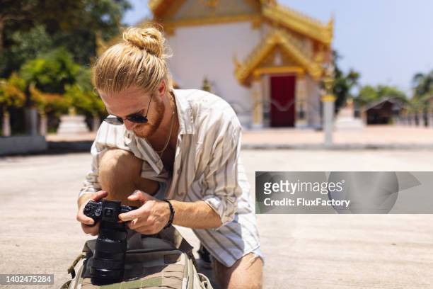 kaukasischer männlicher fotograf, der die fotos vor der kamera betrachtet, die er während seines urlaubs gemacht hat - camera bag stock-fotos und bilder