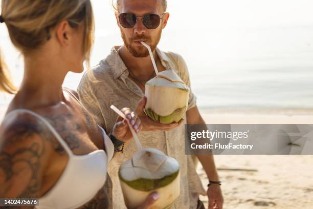 caucasian couple drinking coconut on the beach - coconut stock pictures, royalty-free photos & images