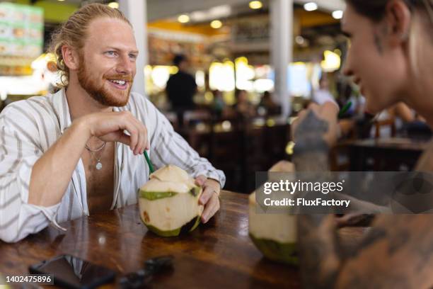 carefree caucasian couple drinking coconut at the modest thai restaurant - kokosmelk stockfoto's en -beelden