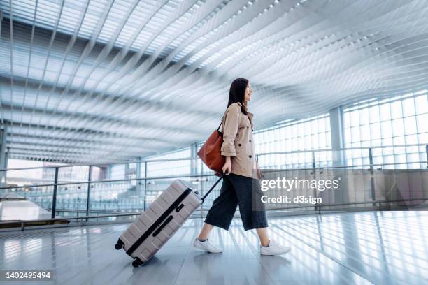 side view of young asian woman carrying suitcase walking in airport terminal. ready to travel. travel and vacation concept. business person on business trip - mala de rodinhas - fotografias e filmes do acervo