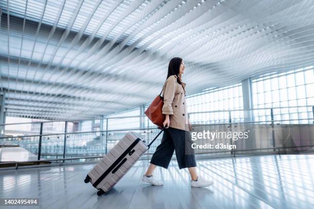 side view of young asian woman carrying suitcase walking in airport terminal. ready to travel. travel and vacation concept. business person on business trip - wheeled luggage 個照片及圖片檔