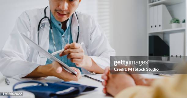 close up of mature asian man doctors medical results during consultation on tablet computer with woman patient in health clinic. - medische testuitslag stockfoto's en -beelden