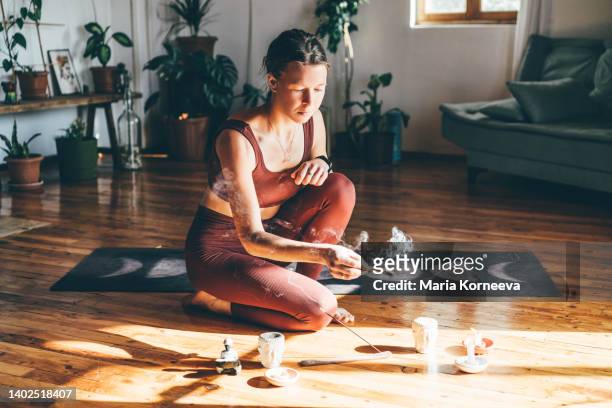 young woman lights a palo santo stick from a candle before meditation. - ceremony stockfoto's en -beelden