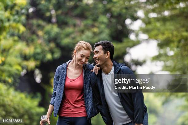 young multiracial couple taking rest break while jogging around suburban housing estate - asian couple exercise stock pictures, royalty-free photos & images