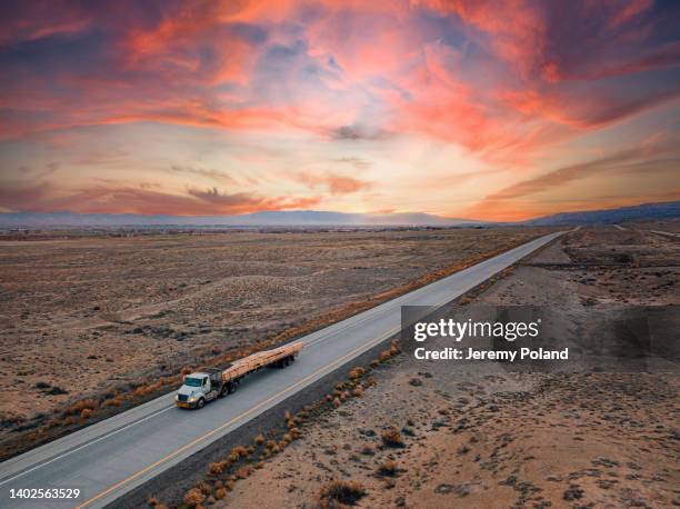 aerial drone shot of a semi truck carrying lumber roof truss materials to build a housing development with a colorful sunset - convoy stock pictures, royalty-free photos & images