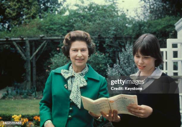 Queen Elizabeth II, wearing a green jacket with a green-and-white scarf, with her niece Sarah Armstrong-Jones, who holds an document in her hands,...