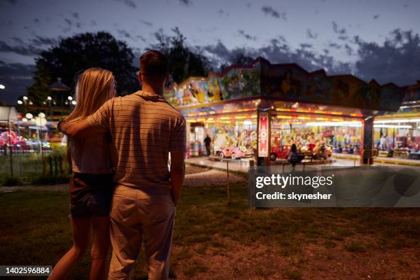 Vista Trasera De La Pareja Abrazada Caminando En El Parque De Diversiones Por La Noche Foto de stock - Getty Images Vista Trasera De La Pareja Abrazada Caminando En El Parque De Diversiones Por La Noche Foto de stock - Getty Images