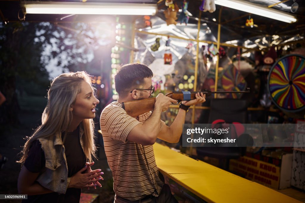 Young man shooting at target while being with his girlfriend at amusement park.