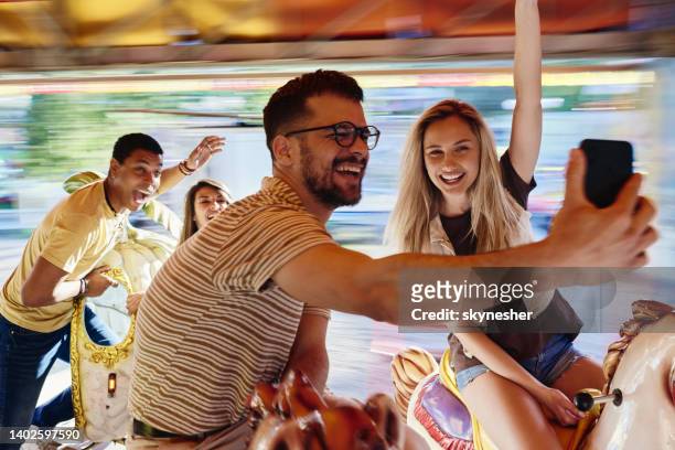 happy friends taking a selfie during carousel ride at amusement park. - festival selfie stock pictures, royalty-free photos & images