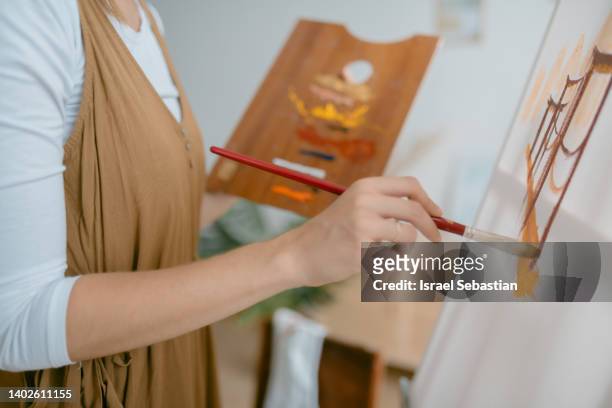 crop of unrecognizable painter standing with colorful paints on wooden palette painting a canvas in art studio - oil painting people stock pictures, royalty-free photos & images