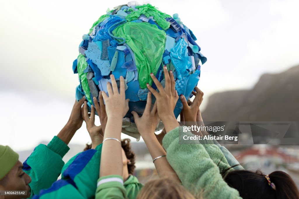 Group of teenagers holding up a world made of plastic trash