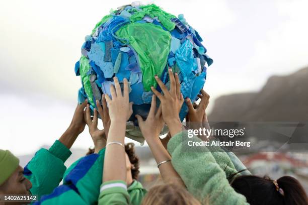 group of teenagers holding up a world made of plastic trash - klima stock-fotos und bilder