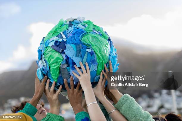 group of teenagers holding up a world made of plastic trash - arts club stock pictures, royalty-free photos & images